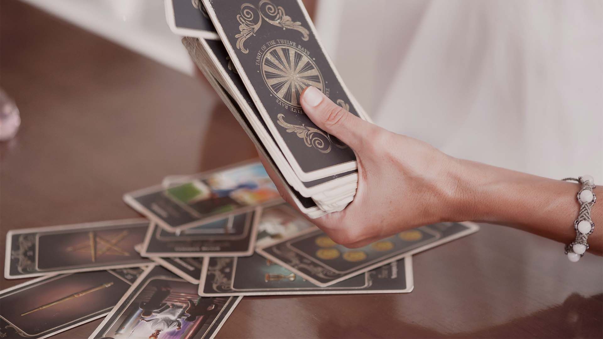 Hand holding a deck of tarot cards above a table with several tarot cards spread out.