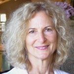 Smiling middle-aged woman with curly gray hair in a warmly lit indoor setting.