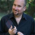 Smiling man with light skin, short hair, and a goatee, wearing a black shirt outdoors.