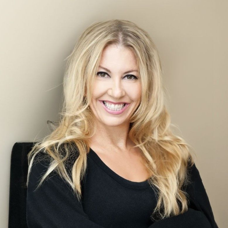 Smiling woman with long blonde hair wearing a black top against a beige background.