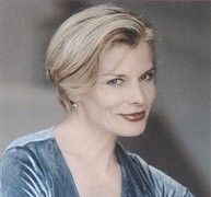 Portrait of a woman with blonde hair wearing a blue velvet top and smiling slightly.
