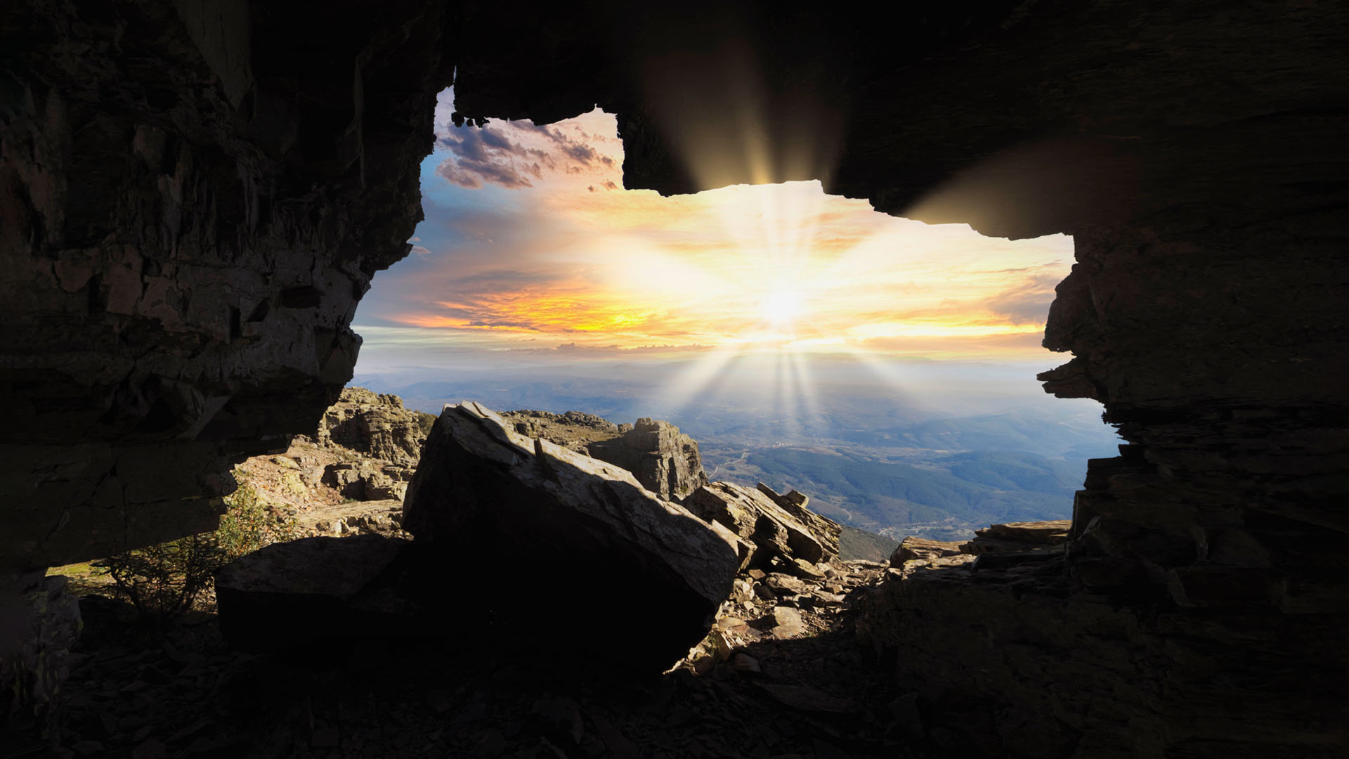View of a rocky mountainous landscape and distant valleys at sunset, seen through a cave opening.