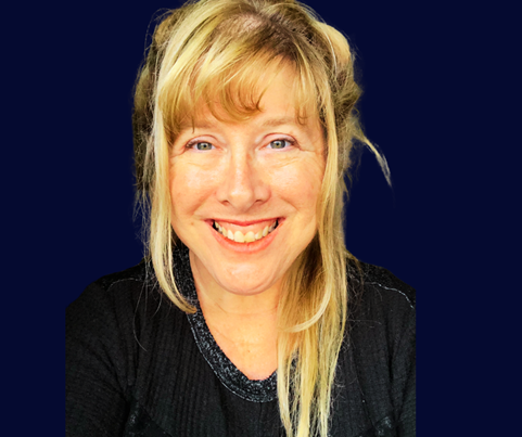 Smiling woman with blonde hair and bangs wearing a black top against a dark blue background.