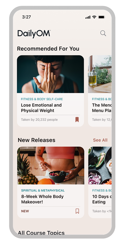 Mobile app screen of DailyOM showing 'Recommended For You' courses including 'Lose Emotional and Physical Weight' with a woman touching her nose, and 'New Releases' featuring '8-Week Whole Body Makeover!' with a person eating a healthy meal.